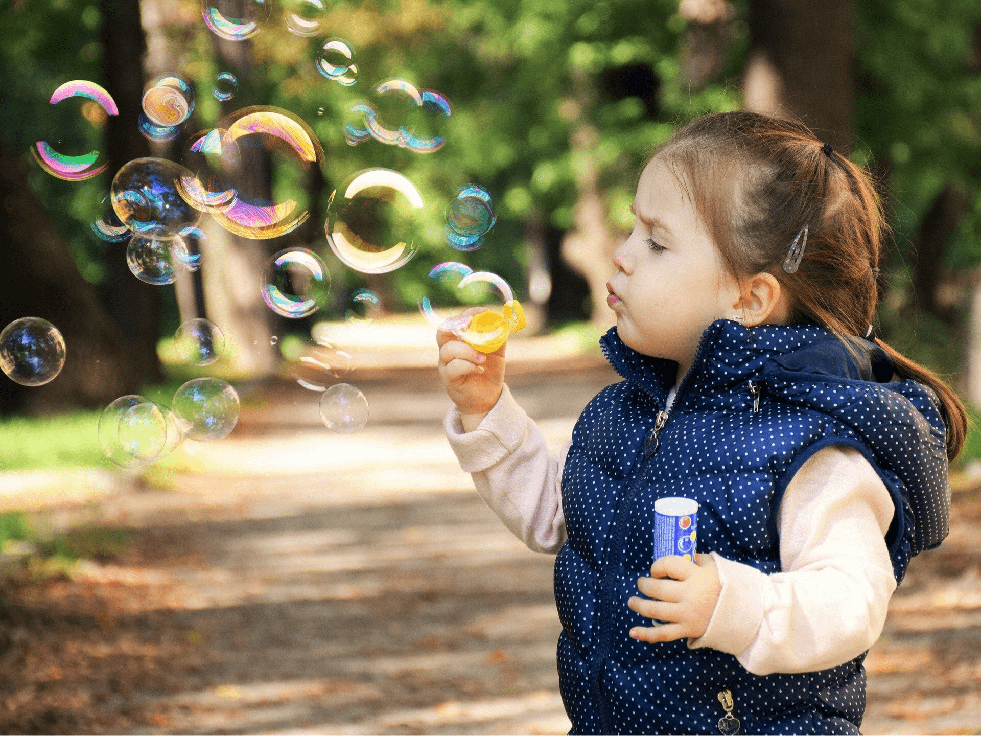 Little girl blowing bubbles outdoors on a wooded path at Wooden Shoes Child Care Center